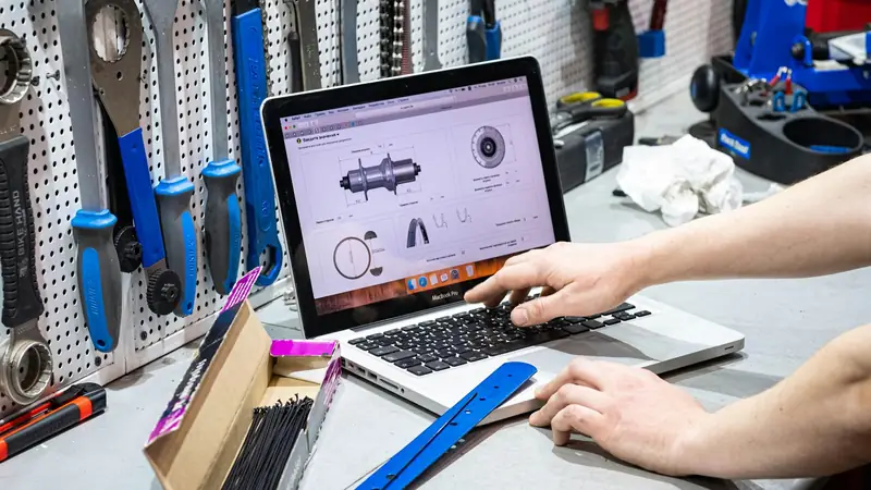 Mann arbeitet am Laptop in einer Werkstatt, umgeben von Werkzeug